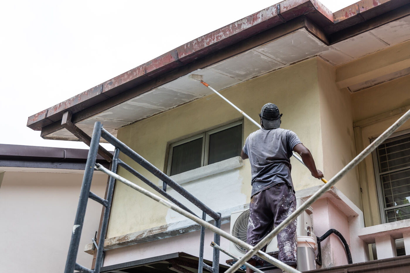 Painter brushing exterior trim from scaffolding, house painting in Winter Haven FL
