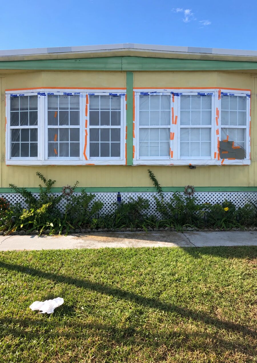Home exterior before repainting, faded yellow siding with green trim and windows masked off for paint, Polk County FL